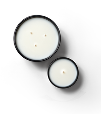 Editorial aerial shot of Standard and Magnum Candles. AMagnum is featured on the left with 3 wicks and standard is featured on the right with one wick. Both candles are against a neutral background.